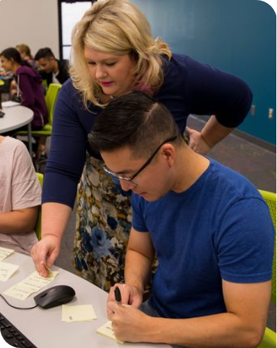 Carrasquilla standing next to a student who is seated and pointing out something on a paper the studentis working on